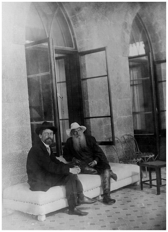 Anton Chekhov and Leo Tolstoy sitting together on a bench in Yalta, Crimea in 1901, both elderly men in dark clothing against a backdrop of arched windows